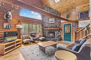 A log cabin interior with a stone fireplace, wooden furniture, and a mounted deer head. - Riverfront Log Cabin "River Chant Lodge" Hot Tub, on the River, Fire Pit; Under New Management (Red River)