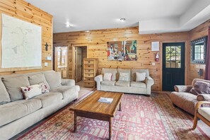 A cozy living room with a wooden wall, a sofa, a coffee table, and a patterned rug. - Riverfront Log Cabin "River Chant Lodge" Hot Tub, on the River, Fire Pit; Under New Management (Red River)