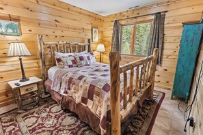 Ein Schlafzimmer einer Holzhütte mit einem Bett, Nachttischlampen, einem Teppich und einem Fenster mit Vorhängen.