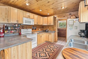A kitchen with wooden cabinets, a microwave, stove, and a sink. - Riverfront Log Cabin "River Chant Lodge" Hot Tub, on the River, Fire Pit; Under New Management (Red River)