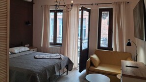 Un dormitorio con cama, sofá, una mesita y una ventana con cortinas.