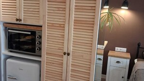 Una cocina compacta con horno integrado, un refrigerador pequeño y gabinetes de madera con puertas persianas.