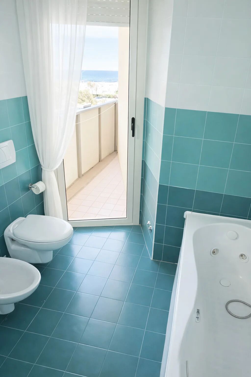 A bathroom with a toilet, bathtub, and a view of the sea through a door.