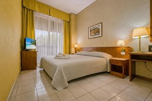 A hotel room with a bed, a desk, a chair, a television, and a window with curtains. - Hotel Remin Plaza (Rimini)