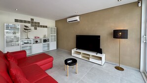 A modern living room with a red sofa, a TV on a white stand, a small black table, and a floor lamp. - Vilamoura Deluxe 2 With Pool by Homing (Loulé)