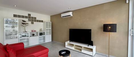 A modern living room with a red sofa, a TV on a white stand, a small black table, and a floor lamp.
