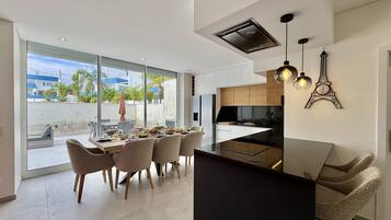 Una cocina moderna con una isla central, una zona de comedor con seis sillas y un amplio ventanal con vistas a un barrio residencial.