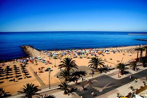 Una playa con sombrillas, palmeras y un cielo azul despejado.