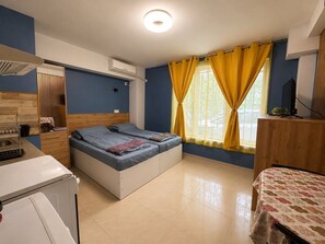 Ein kleiner Raum mit Bett, Schreibtisch, Waschmaschine und einem fensterbepflanzten Fenster.