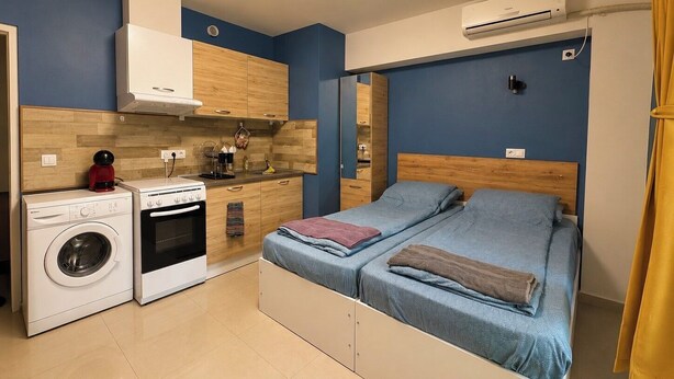 Ein kleines Zimmer mit Bett, Waschmaschine, Herd und einer kleinen Küchenzeile.