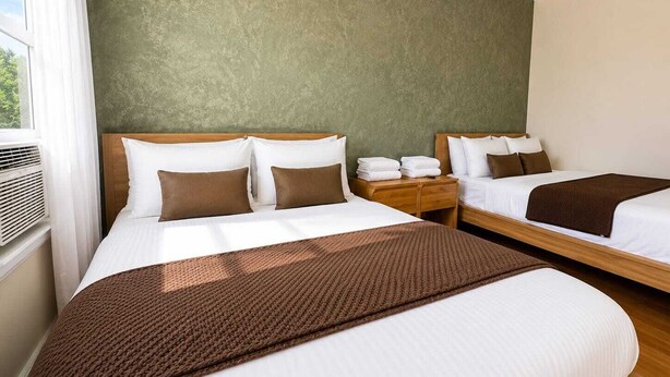 Een hotelkamer met twee bedden, een houten hoofdeinde, een groene wand en een raam met gordijnen.