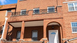 A red brick building with a white door, a covered porch, and a small balcony.