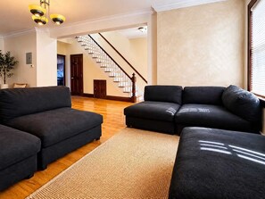 Ein Wohnzimmer mit dunklen Sofas, Holzboden, einer Treppe und einer Pflanze.