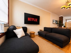 A living room with a black sofa, a small round table, and a TV mounted on the wall displaying 'NETFLIX'.