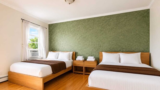 A hotel room with two beds, a green accent wall, wooden flooring, and a window with curtains.