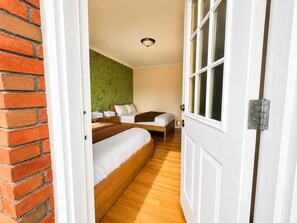 A hotel room with a brick wall, a green accent wall, wooden flooring, two beds, a window, and a door with a metal handle.
