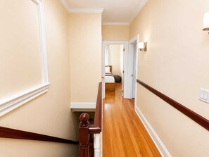A hallway with wooden trim, a staircase with a handrail, and a bed in the distance.