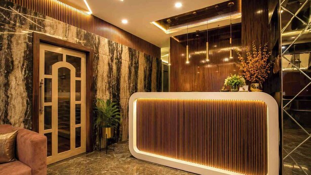 A reception area with a marble wall, a wooden reception desk, and a leather sofa. - Royal  Chandra Hotels (Patna)