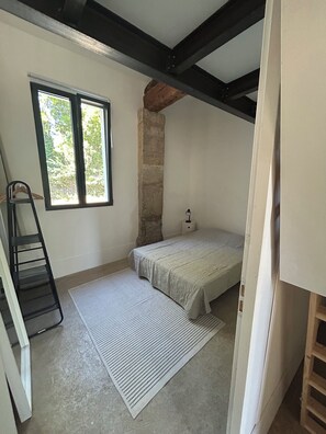 A bedroom with a bed, a window, a ladder, and a stone wall. - Charming Artist’s House with Private Gardenparking  near Narbonne City Centre (Narbonne)