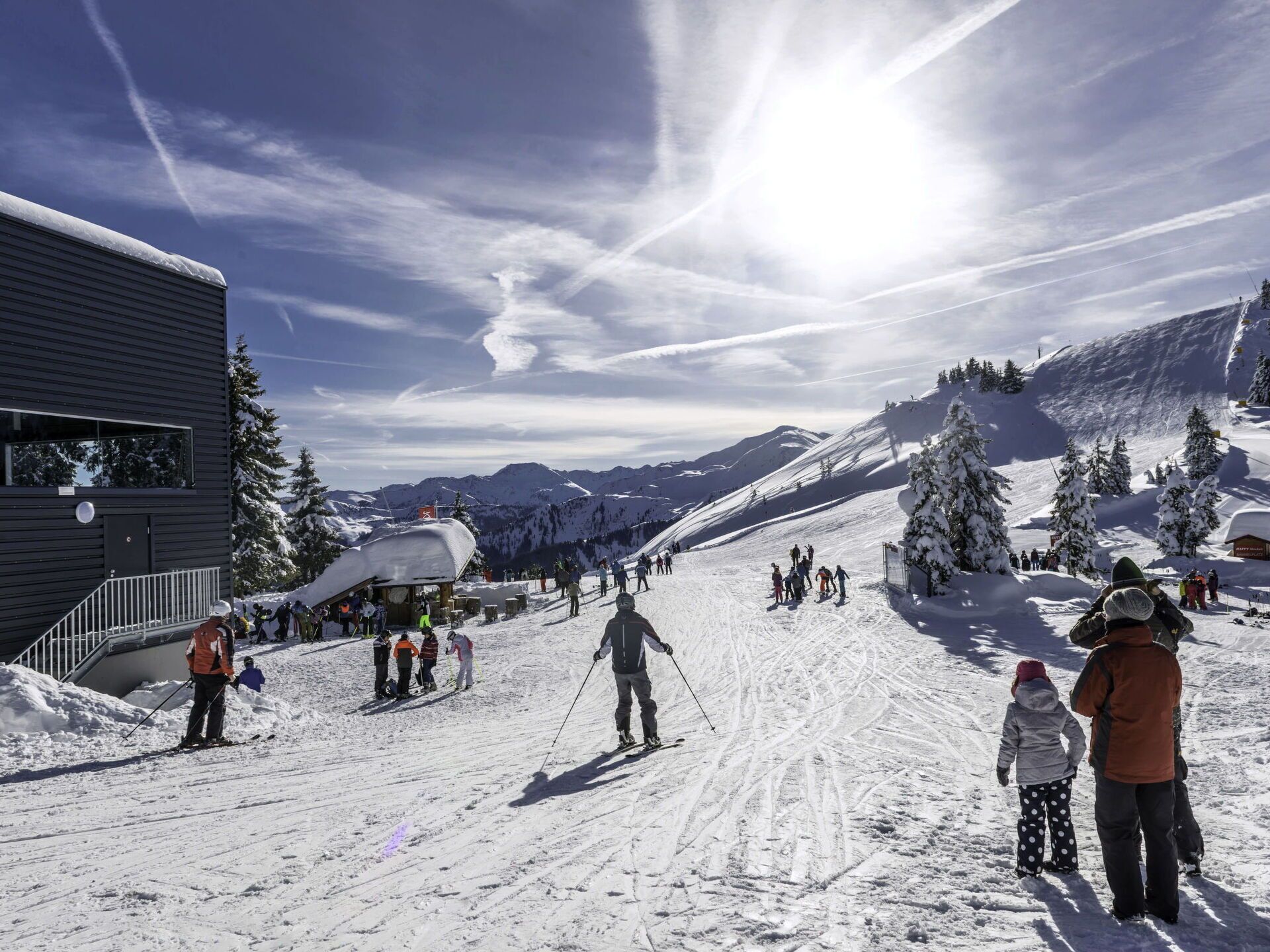 Een wintersportgebied met blauwe lucht, besneeuwde hellingen en een gebouw met een schuin dak.