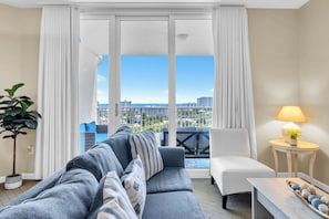 A living room with a sofa, a chair, a lamp, and a view of the city through large windows. - Sun, Sand & Gulf Views | End of Summer 15% off (Destin)