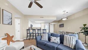 Ein Wohnzimmer mit Sofa, Couchtisch mit Dekoration, Deckenventilator und einem Essbereich mit Stühlen und Tisch.