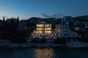 A coastal hotel with a prominent building, a pool, and a view of the sea.