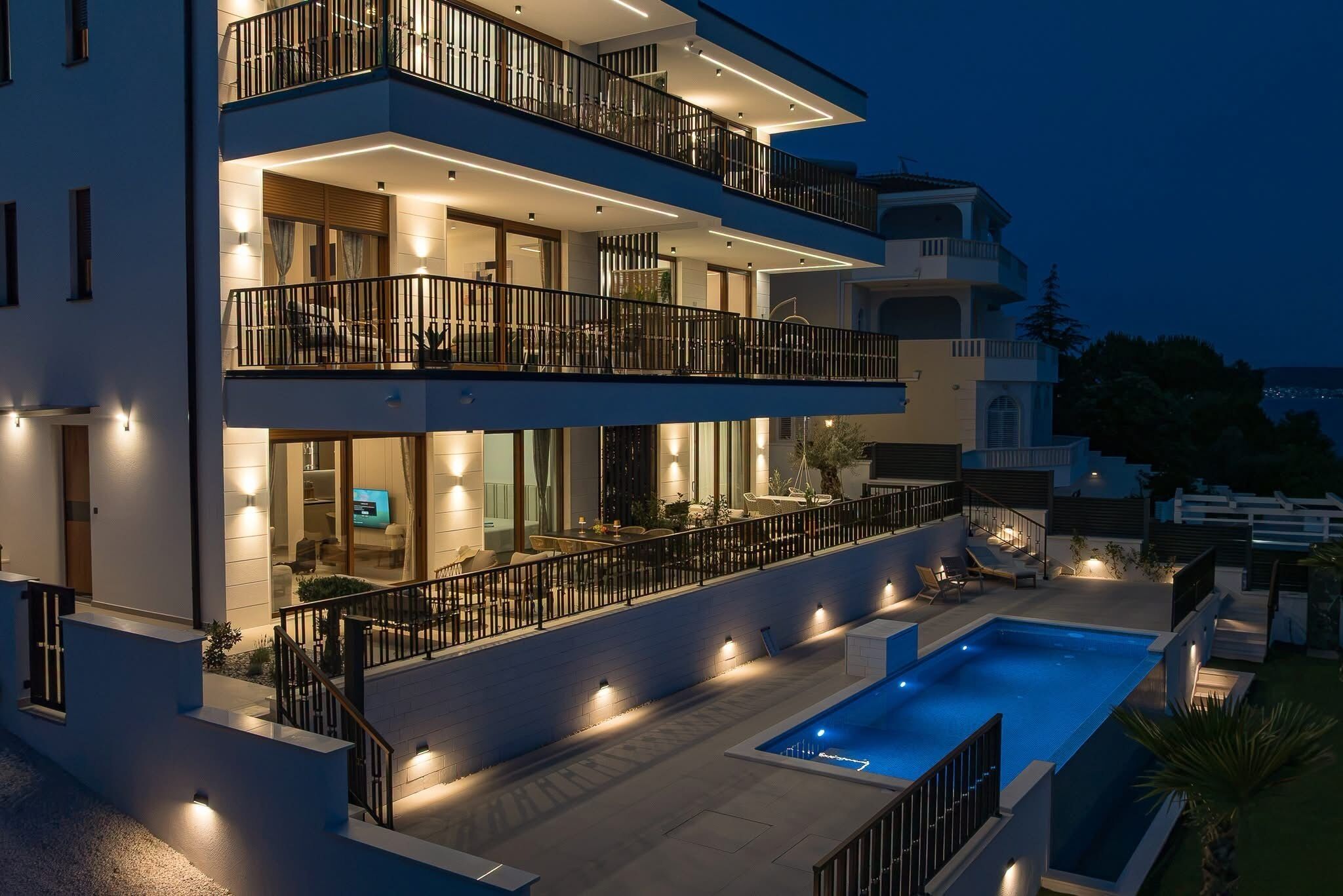 Un edificio de varios pisos con piscina, balcones e iluminación exterior.