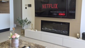 Una sala de estar moderna con un televisor de pantalla plana montado en la pared, una chimenea abajo y una mesa de centro de mármol con un jarrón decorativo.