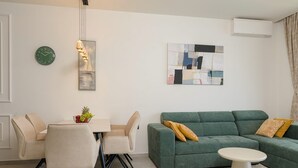 Una sala de estar moderna con un sofá verde, una mesa de comedor con sillas, una mesa de centro blanca y un reloj de pared.