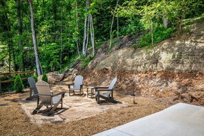 An outdoor seating area with Adirondack chairs and a table, surrounded by a forested hillside. - Tennessee Sunrise | Mountain Views, 3 King Suites, WifFi & Games (Sevierville)