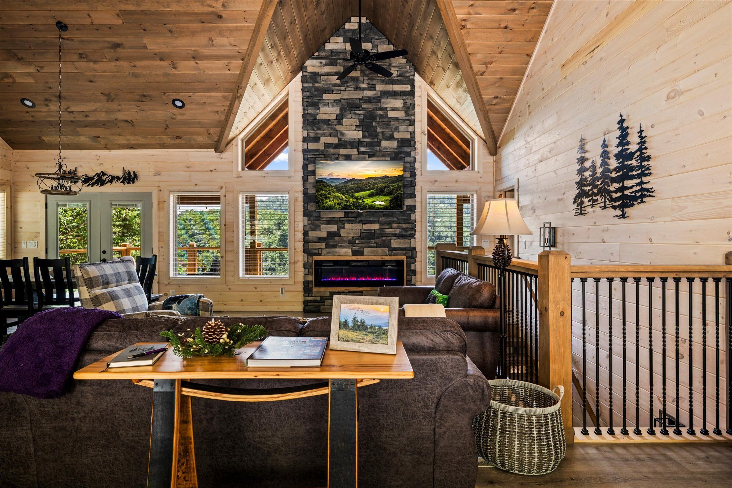 A cozy living room with a stone fireplace, wooden ceiling, and a view of the outdoors.