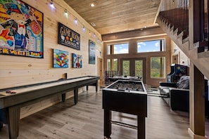 A room with a foosball table, a pool table, and a billiards table. There are large windows and a wooden ceiling. - Tennessee Sunrise | Mountain Views, 3 King Suites, WifFi & Games (Sevierville)