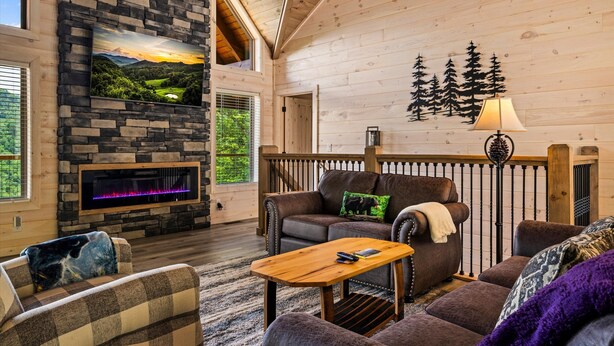 A cozy living room with a stone fireplace, a large window overlooking a scenic landscape, and a wooden ceiling. - Tennessee Sunrise | Mountain Views, 3 King Suites, WifFi & Games (Sevierville)