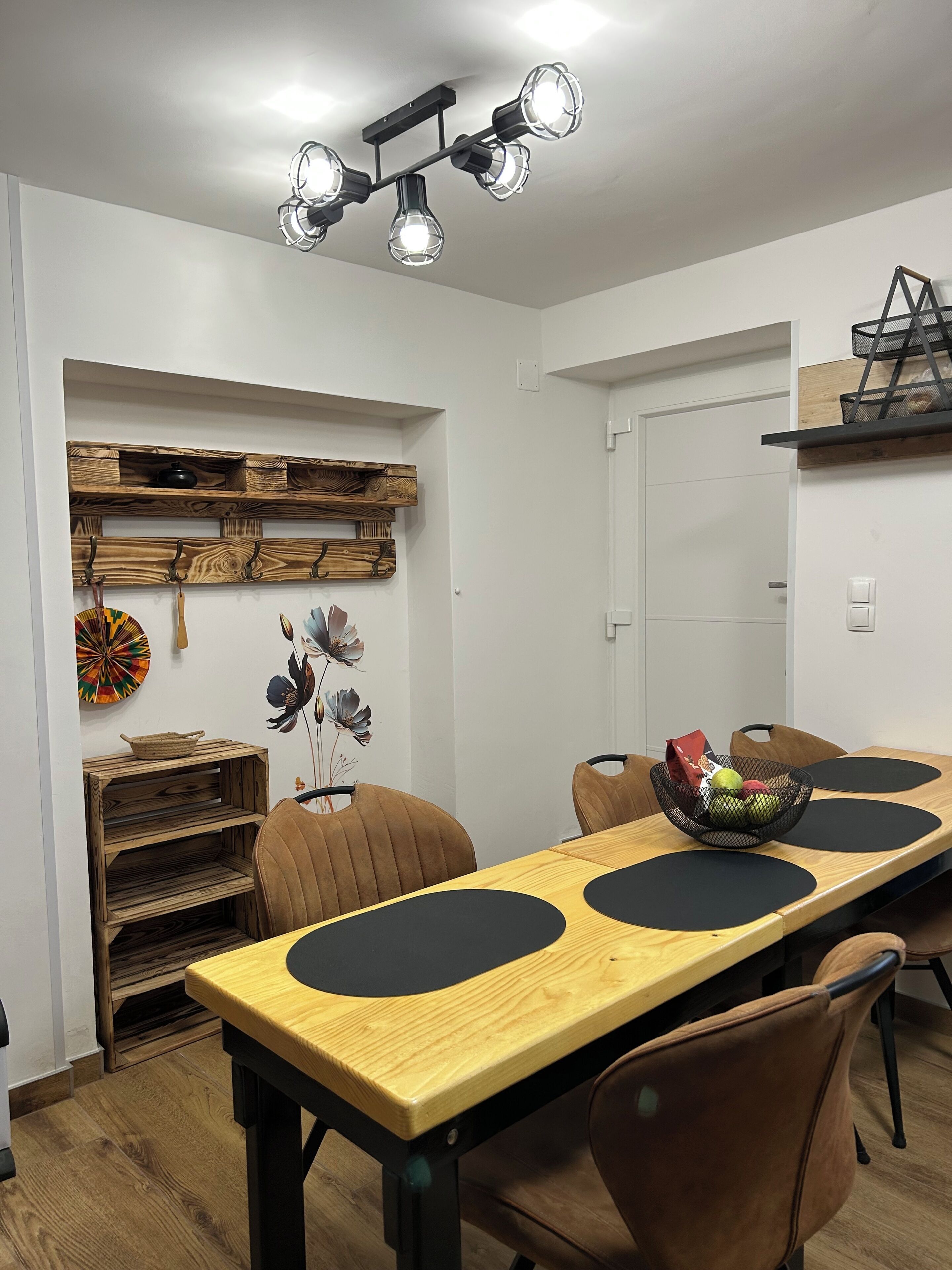 Un comedor con una mesa de madera, sillas, una lámpara en el techo y un estante fijado a la pared.