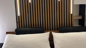 Habitación de hotel con cama, dos almohadas, pared de listones de madera y un altavoz.