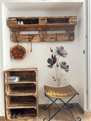 A corner room with a wooden shelf unit, a wall-mounted clock, a decorative plate, a floral mural, and a foldable stool. - Ljubica House (Vodice)
