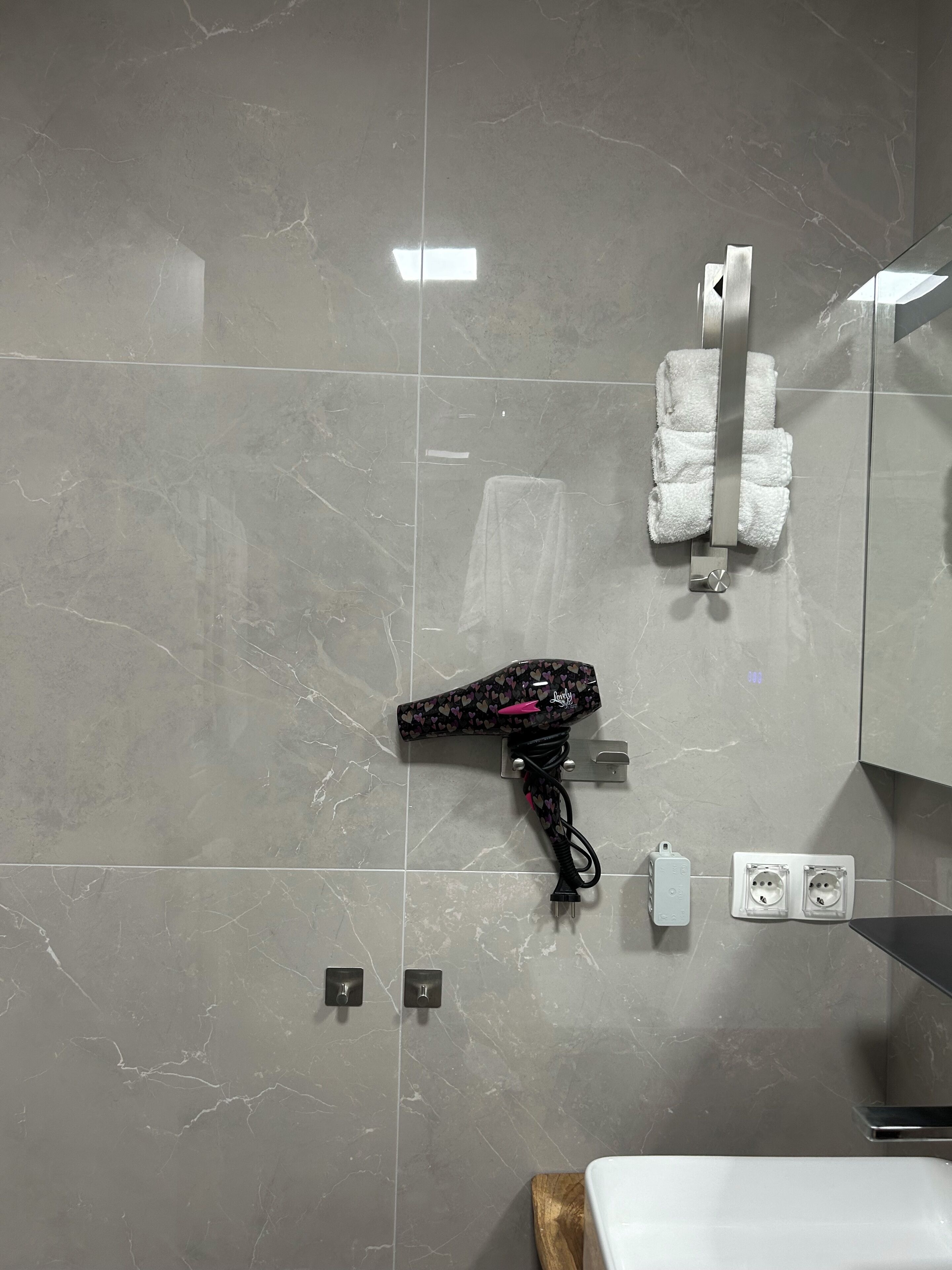 Ein Badezimmer mit Marmorwand, einem Föhn an einer Wandhalterung, einem Handtuchhalter mit weißen Handtüchern und einem Waschbecken mit Holzbeschlag.