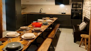 Une cuisine avec une longue table en bois, dressée pour le repas, et équipée de différents plats et ustensiles.