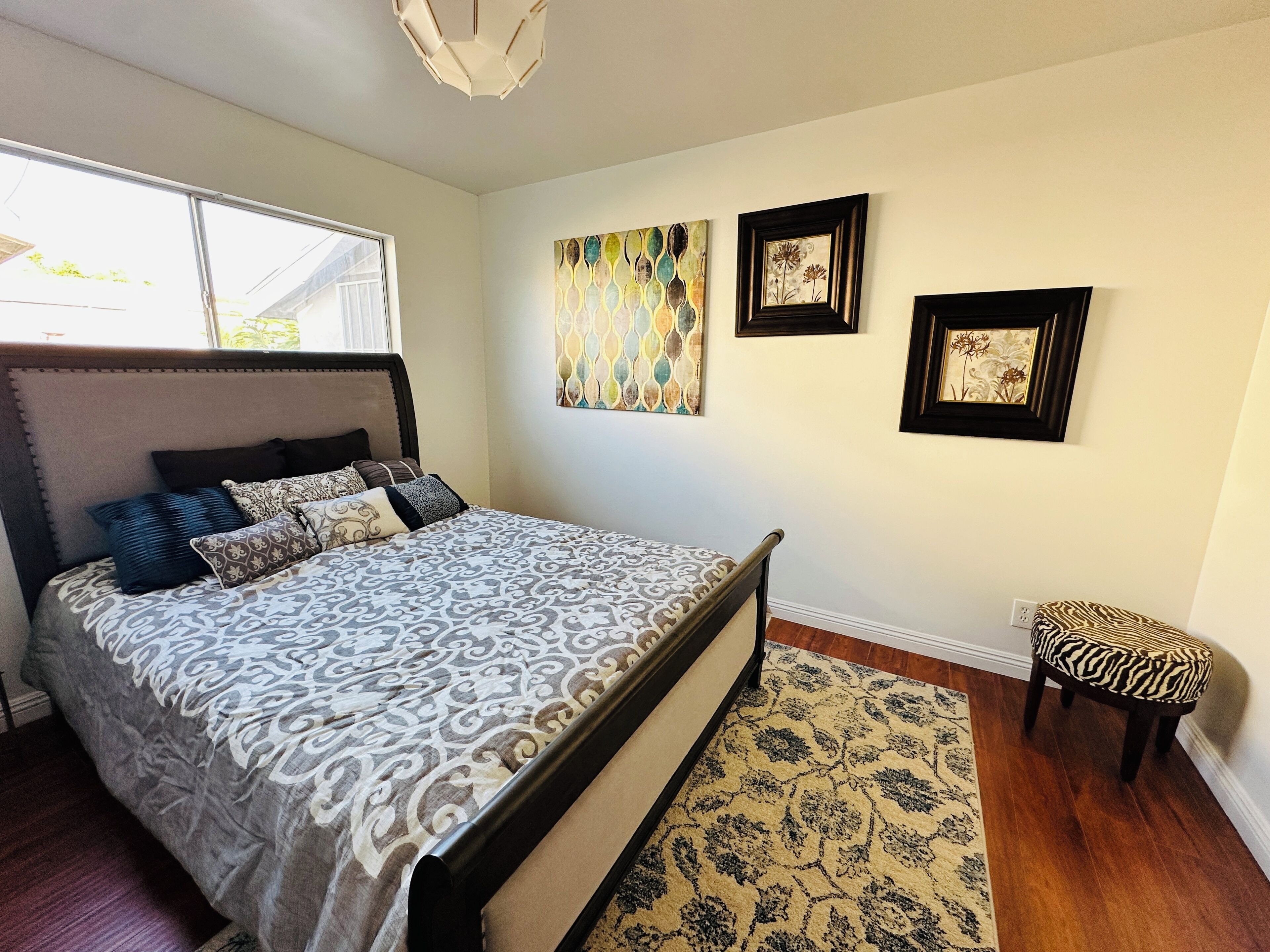 A bedroom with a bed, a rug, a chair, and artwork on the wall.