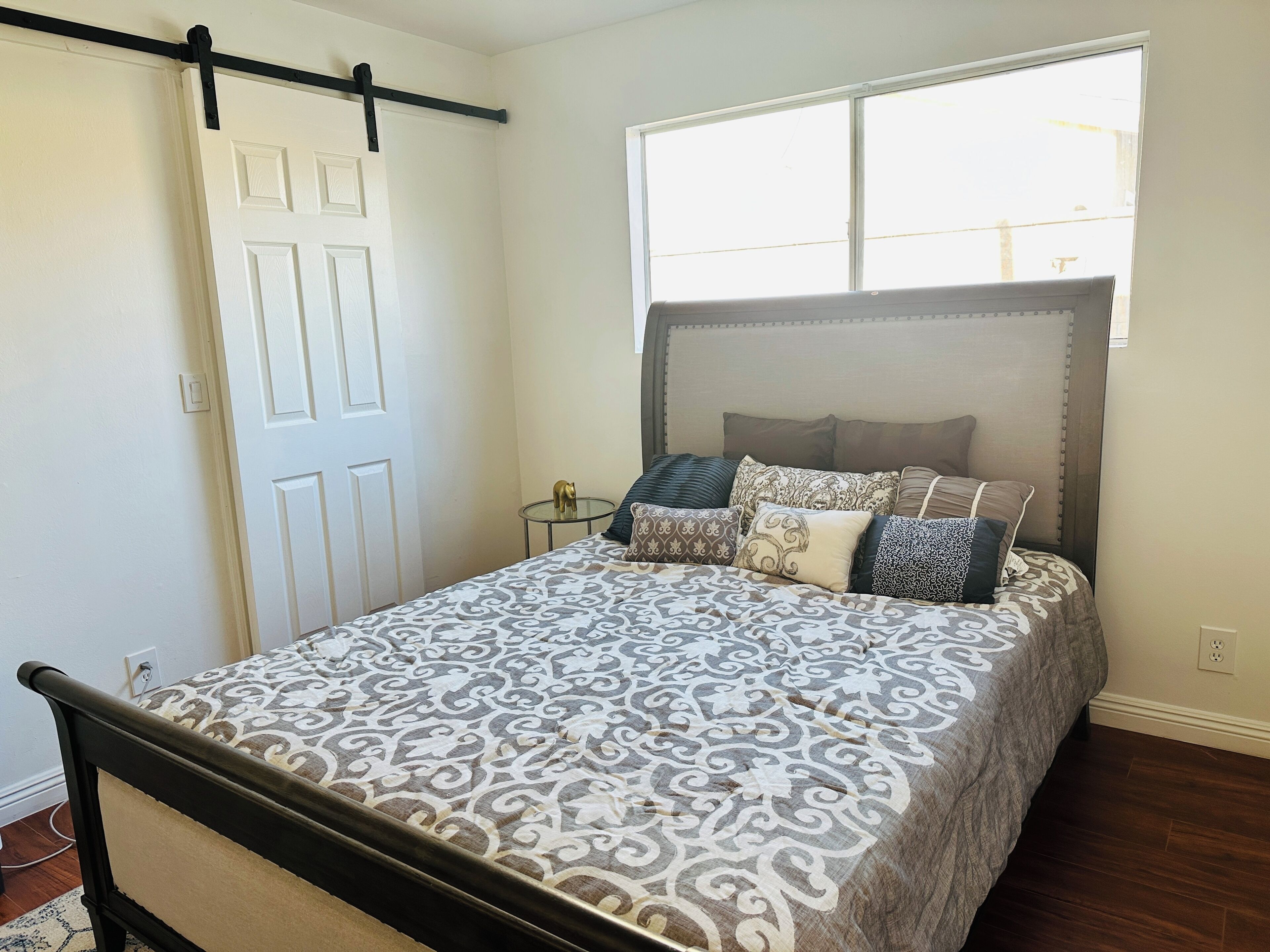 Une chambre à coucher avec un lit, une fenêtre, une porte et une petite table sur laquelle se trouve un objet décoratif.