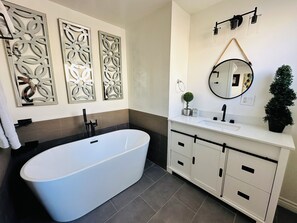 Ein modernes Badezimmer mit einer freistehenden Badewanne, einem Waschtisch mit Spiegel und dekorativen Wandverkleidungen.