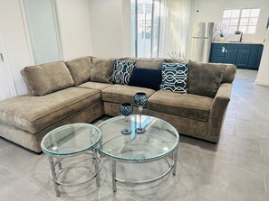 Ein Wohnzimmer mit einem Ecksofa, zwei Glastischen und dekorativen Kissen.