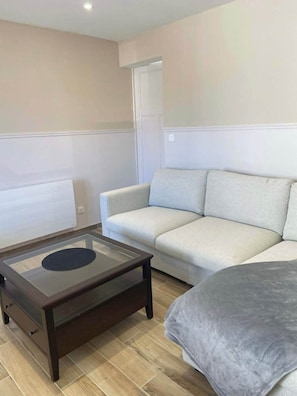A living room with a sofa, a glass-top coffee table, and a door. - Le Bruit des Vagues, an apartment 50 meters from the ocean (Quend)