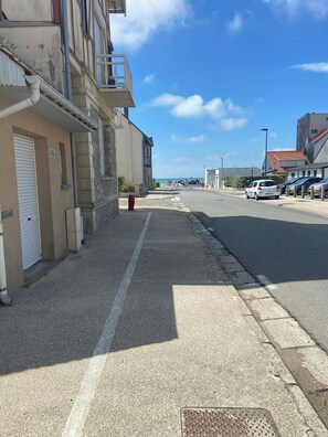 En gatubild med byggnader, en klar himmel och parkerade bilar.