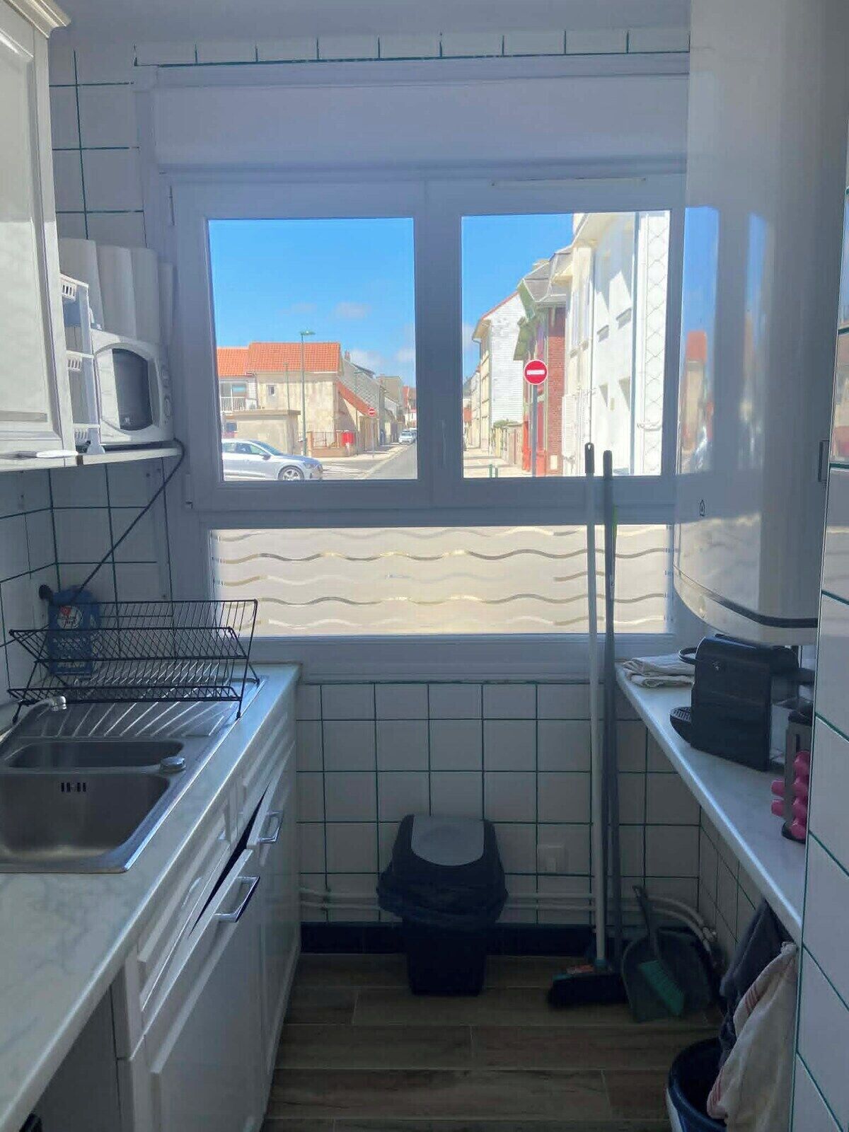 A compact kitchen with a window, a microwave, a sink, and a trash bin.