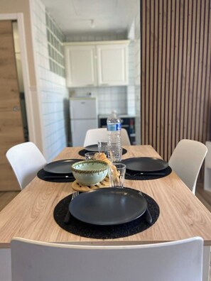 A dining table set with black plates, a bowl, and glasses, with white chairs around it. - Le Bruit des Vagues, an apartment 50 meters from the ocean (Quend)