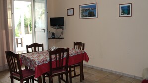 A dining area with a table set for four, chairs, a TV on a stand, and framed pictures on the wall. - Terra di Mare: Three-room apartment (sub5) with a large garden, 2 km from the sea (Vignacastrisi)