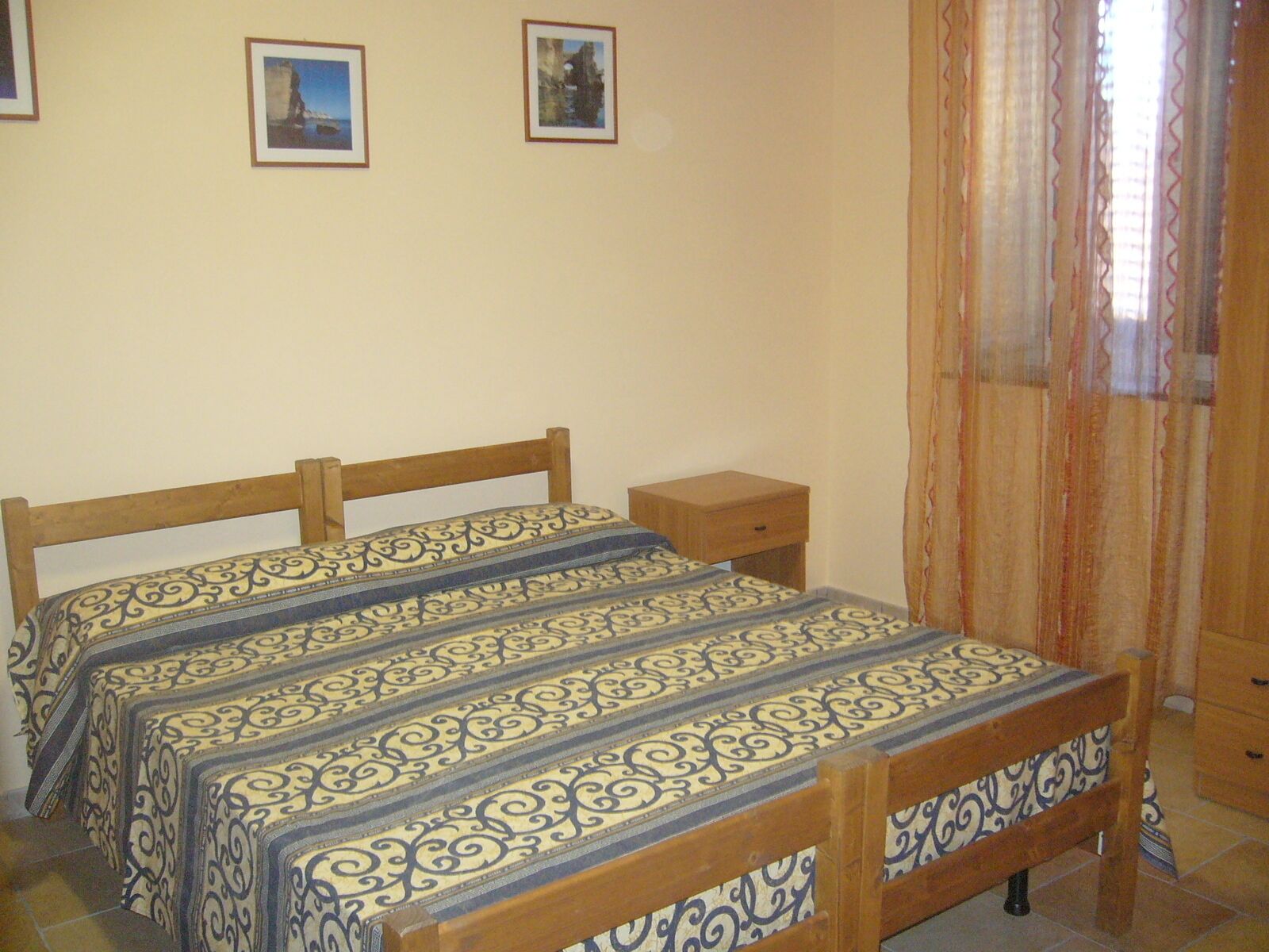 A bedroom with two beds, a wooden nightstand, and a window with curtains.