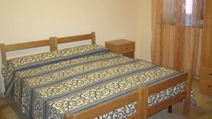 A bedroom with two beds, a wooden nightstand, and a window with curtains. - Terra di Mare: Three-room apartment (sub5) with a large garden, 2 km from the sea (Vignacastrisi)